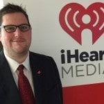 Adam Weiss standing in front of iHeartMedia logo