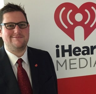 Adam Weiss standing in front of iHeartMedia logo