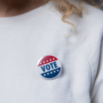 A stock image of a "Vote" button on a woman's t-shirt.