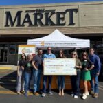 Fresno’s KMJ Turns One Broadcast Day Into 1.7M Meals Group holding a Central California Food Bank donation check in front of The Market in Fresno