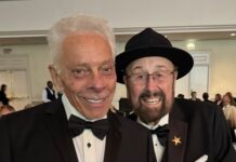 Two men in tuxedos smile at the camera at a banquet