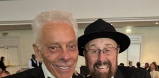 Two men in tuxedos smile at the camera at a banquet