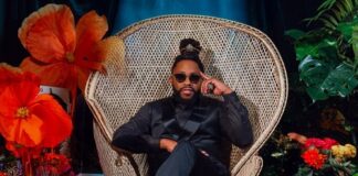 Raheem DeVaughn seated in a wicker chair surrounded by flowers and plants