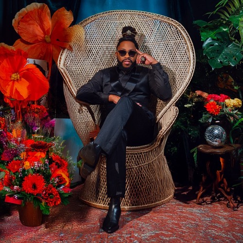 Raheem DeVaughn Raheem DeVaughn seated in a wicker chair surrounded by flowers and plants