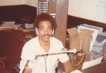 Ronnie Love seated at a microphone in the WJBE studio, wearing headphones